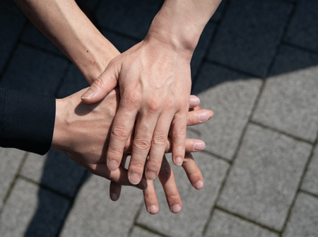 3人がコンクリートの上で手を重ね合わせている写真